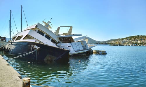 A boat keeling on its side at a dock after another boat collided with it.