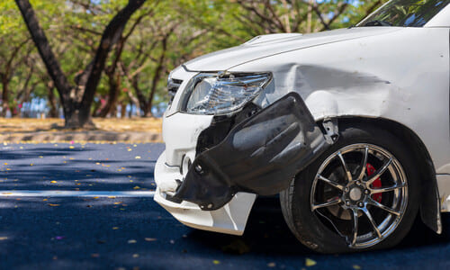 A crumpled front end of a white car after colliding with an object.