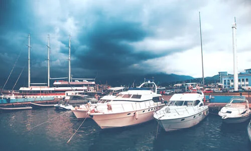 Boats lined up along docks at a marina while dark clouds build overhead.