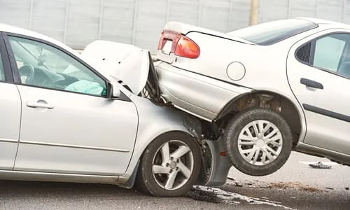 Two grey sedans in a serious rear-end car accident, with the front car resting on the hood of the rear car.