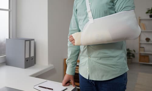 A man standing in an office with an arm cast and sling.