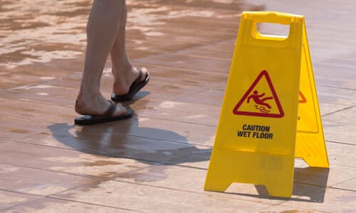 A pair of legs walking past a yellow wet floor warning sign.