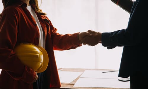 A lawyer in his office shaking hands with a female hard hat worker who decided to work with him.