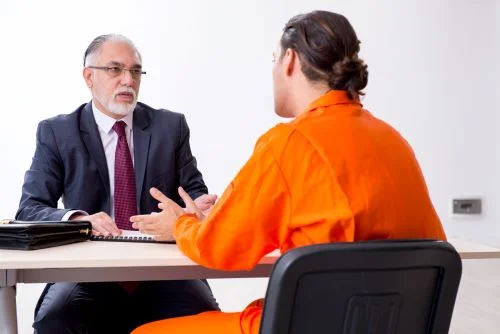 A man in an orange jumpsuit describes his police misconduct case to his personal injury lawyer.