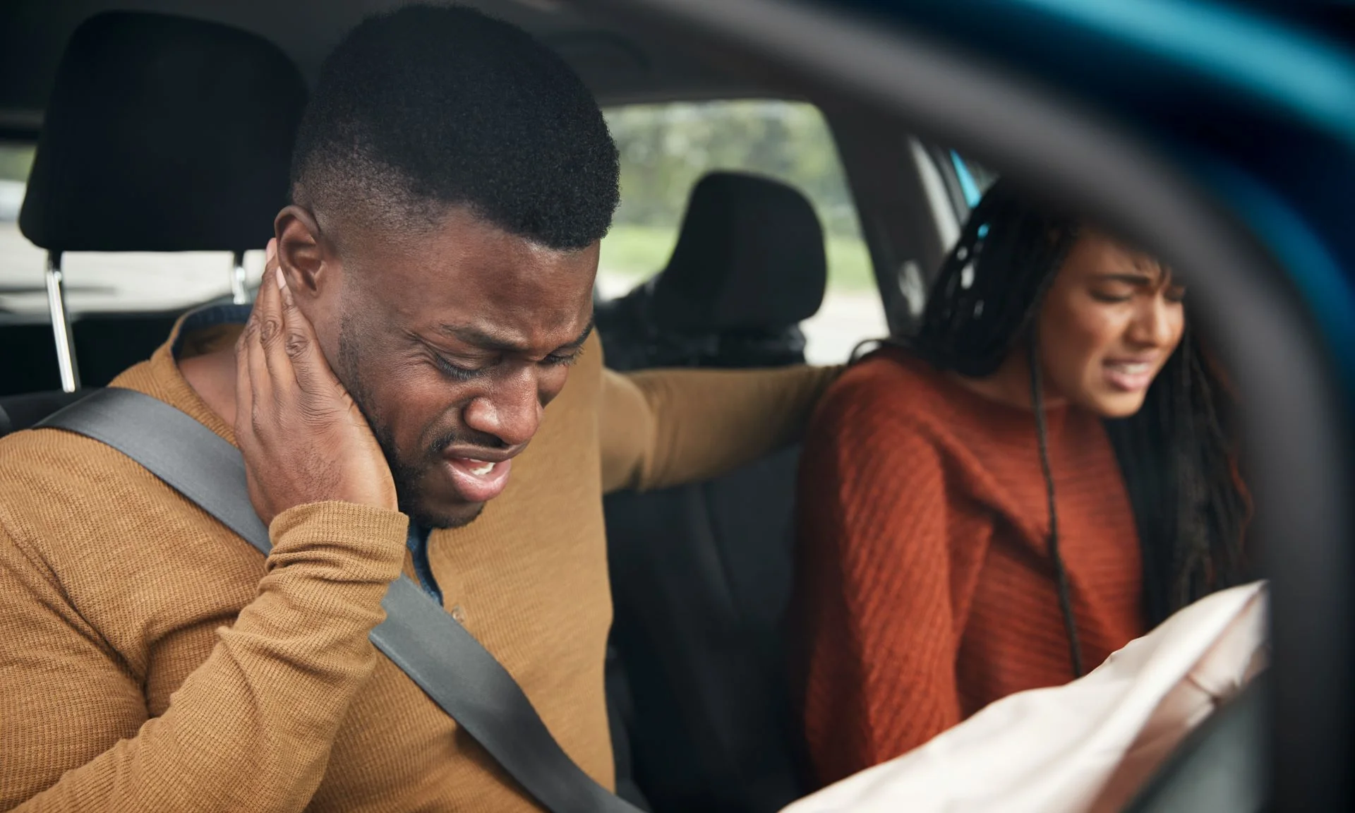 A couple in a car with pained faces after sustaining whiplash in a crash.