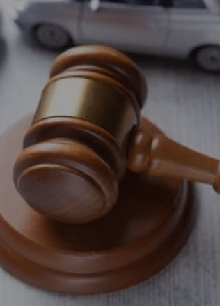 A judge's gavel and soundblock on a table next to two grey toy cars depicting a collision accident.