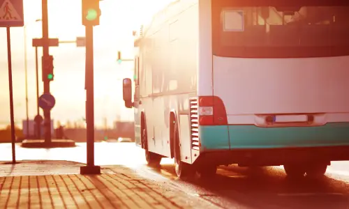 A city bus in the afternoon driving through an intersection after the traffic signal goes green.