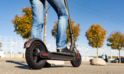 A man in jeans mounting an electric scooter to go on a ride through a city.