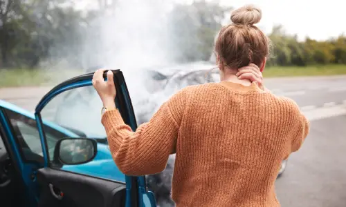 A woman stepping out of a vehicle and holding her neck in pain after an accident.