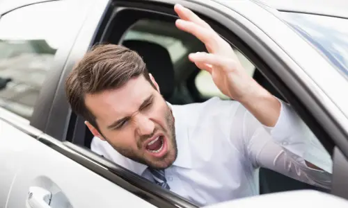 An angry driver with his head out the window yelling at another road user.