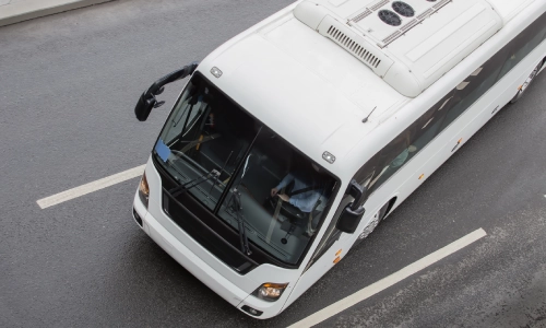 An overhead shot of a white bus on a road about to make a turn.