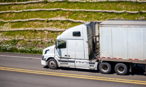 A white semi truck pulling a trailer on a road next to some hills.
