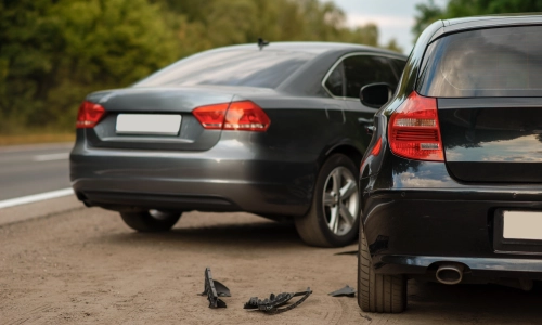 A collision between a grey car and a black hatchback on a rural highway.