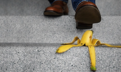A closeup of a man's feet as he goes down a staircase about to slip on a banana peel.