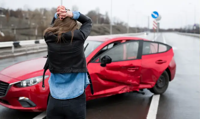 A woman frustrated and standing in front of her crashed red vehicle.